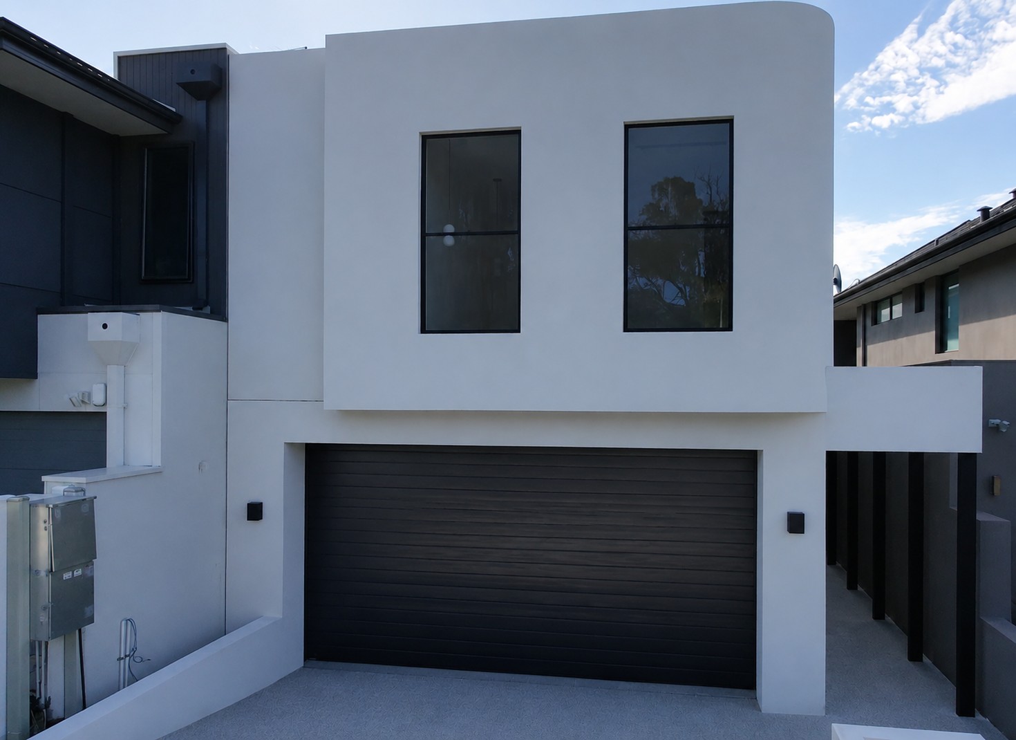 Front of the two-storey Melville home by Skytree Homes, with white render and a black garage door