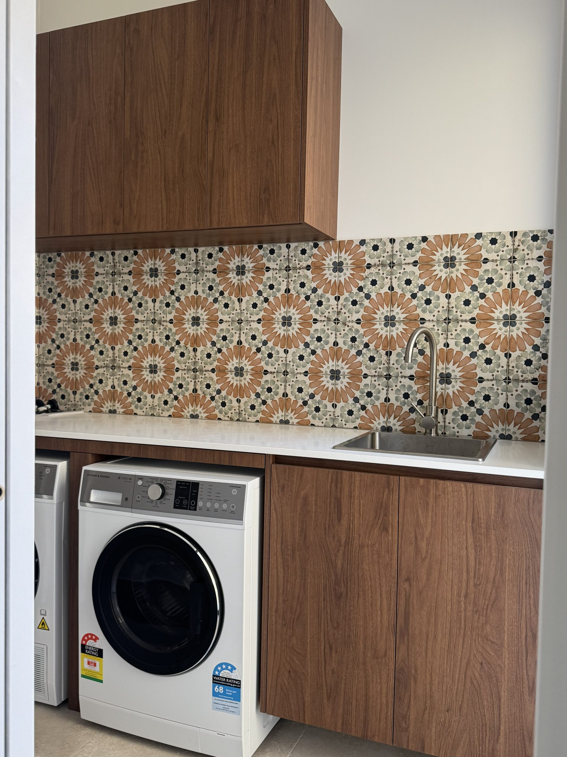Laundry with patterned tile splashback and timber-look cabinetry at the Melville home by Skytree Homes