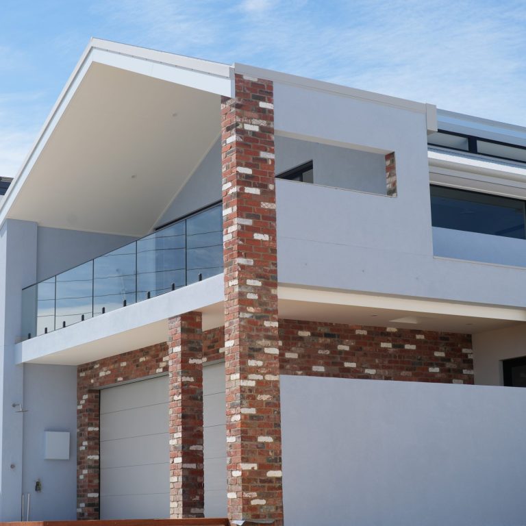 Street view of the two-storey North Coogee home by Skytree Homes, with a red brick feature pier, glass balcony and raked roofline