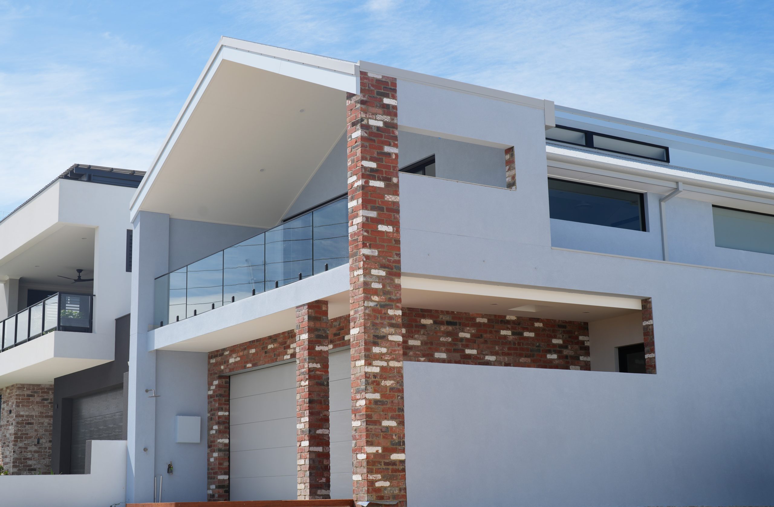 Street view of the two-storey North Coogee home by Skytree Homes, with a red brick feature pier, glass balcony and raked roofline