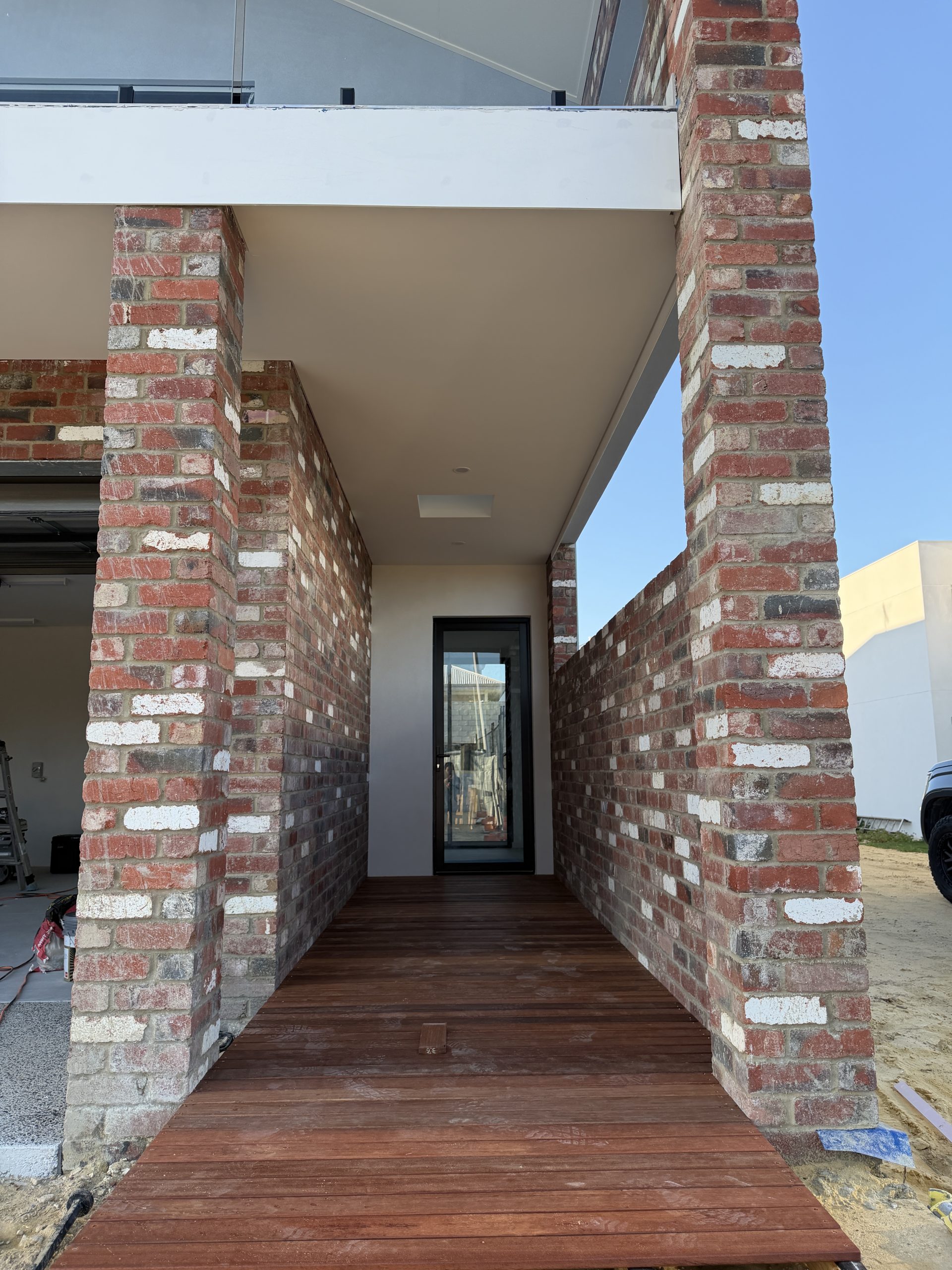 Timber-decked entry walkway between red brick walls at the North Coogee home by Skytree Homes