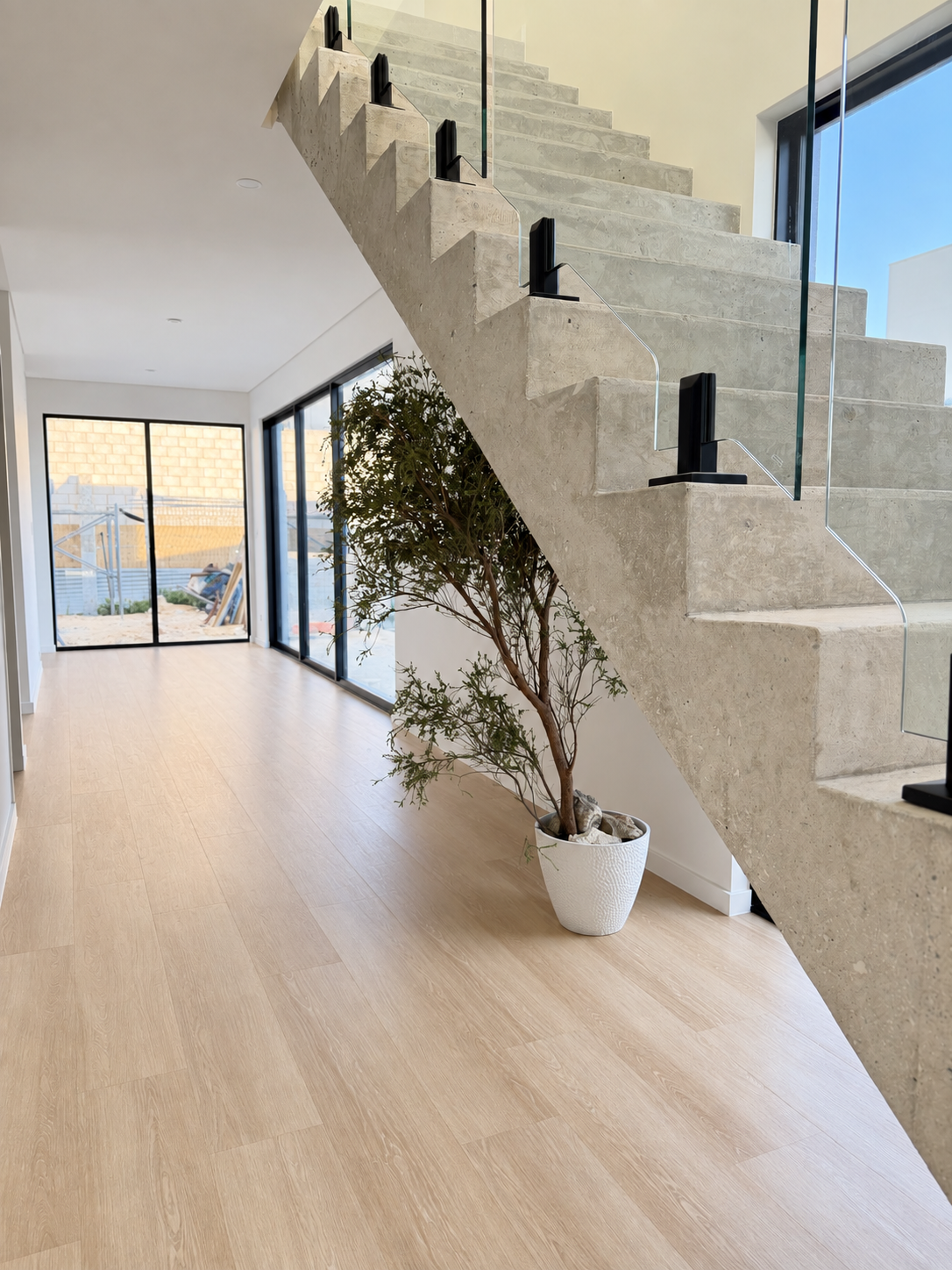 Hallway with timber-look flooring beside a staircase with glass balustrade at the North Coogee home by Skytree Homes