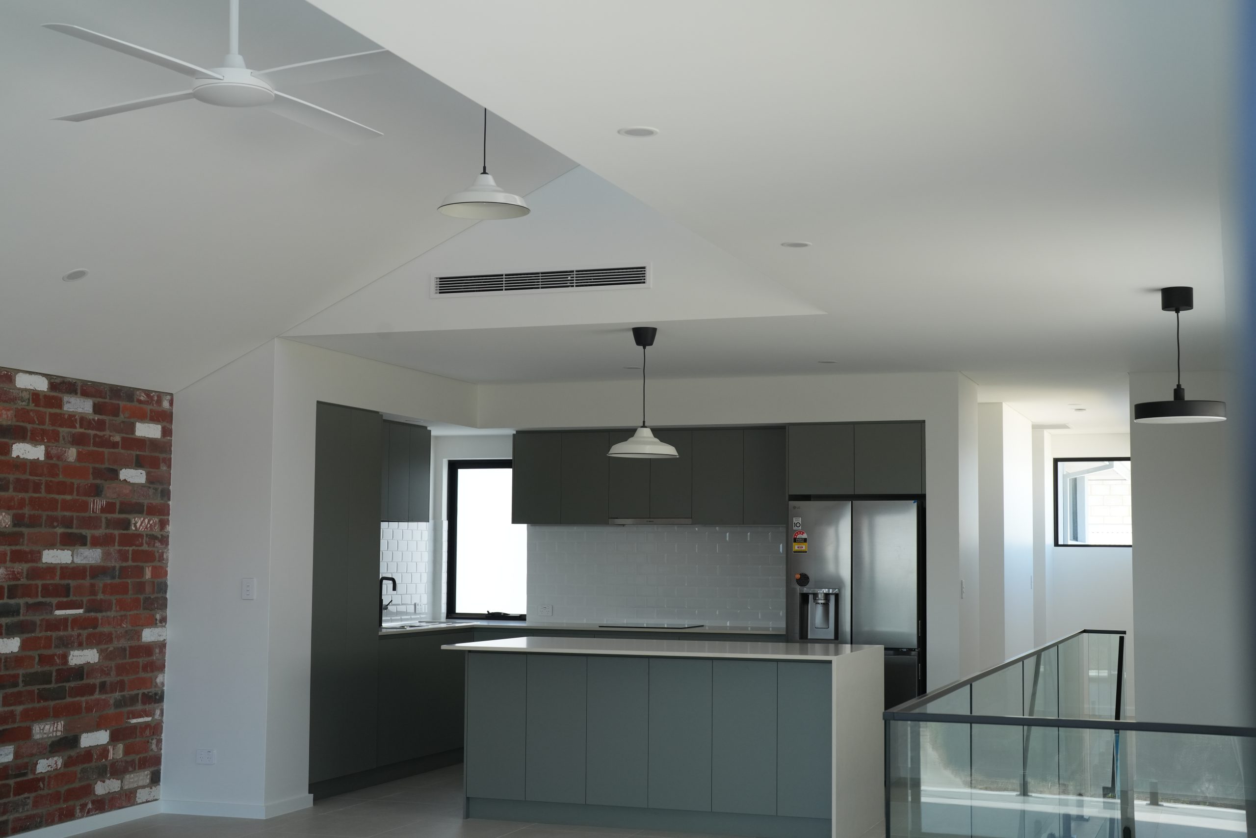 Open-plan kitchen with island bench, pendant lights and red brick feature wall at the North Coogee home by Skytree Homes